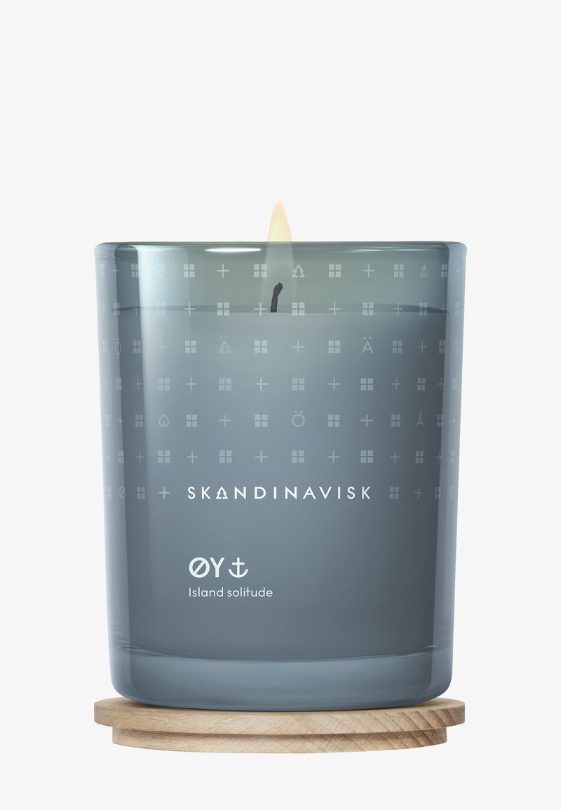 Scented candle in a smoky gray glass container with a wooden base. Features embossed geometric patterns and a visible wick with a flame.
