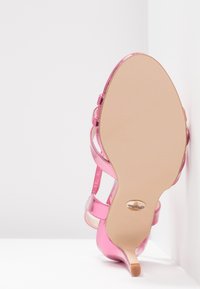 Sandale à talons hauts rose avec un design à lanières, vue de la semelle sur un fond blanc en coin.