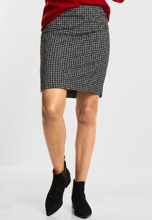 Jupe crayon en noir et blanc à motif pied de poule avec une finition texturée, associée à des bottines noires à bout pointu en suède.