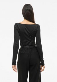 Zwarte longsleeve top met een ruime halslijn, gemaakt van gladde stof, gecombineerd met hoge zwarte broeken met een bijpassende riem en zakken.