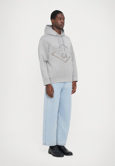 Grijze hoodie met een diamanten logo ontwerp. Gecombineerd met lichtblauwe wijde jeans en zwarte instapschoenen.