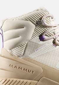 Beżowe buty turystyczne z teksturowaną tkaniną, wzmocnionymi elementami i purpurowymi akcentami. Zawierają logo "DRYTECHNOLOGY" oraz trwały wzór podeszwy.