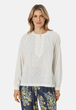 Hvid, tekstureret bluse med lange ærmer og en nøglehul-udskæring, med dekorative knapper og rynkede detaljer ved skuldrene.