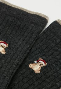 Grå ribbede sokker har et broderet tøjbjørn iført en rød julestråhue. Mansen er i en kontrasterende lys beige.