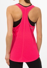 Růžový sportovní top s designem racerback, který má pruhovanou texturu a zakřivený lem. Černá sportovní podprsenka viditelná pod ním.