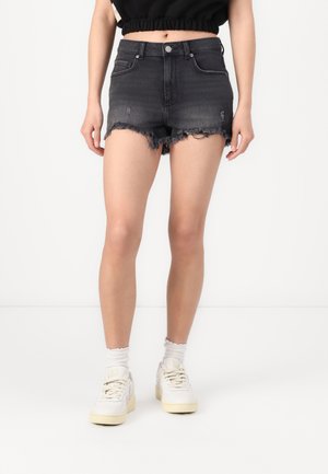 Shorts in denim nero con orlo sfrangiato e dettagli logorati, abbinati a sneakers bianche e calzini bianchi alla caviglia.