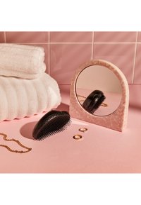 Zwarte ontklitborstel, roze gemarmerde spiegel, witte gestructureerde handdoeken, gouden sieraden, tentoongesteld op een roze oppervlak.