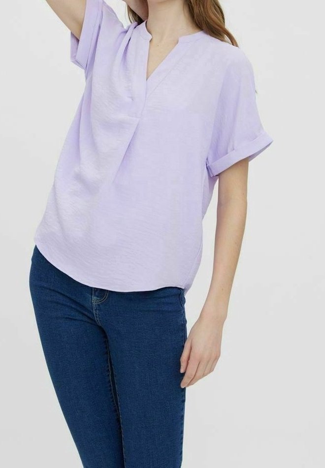 Blouse lilas à manches courtes avec une coupe décontractée, col en V et revers retroussés, associée à un jean denim bleu foncé. Texture lisse.