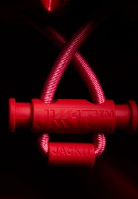 Röd plast snäppknapp med präglad text "JK1T" och "JACK1T", tillsammans med tjock rosa flätad snöre, mot en svart bakgrund.