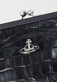 Clutch din piele ecologică de crocodil neagră, cu un închizător metalic ce prezintă un emblemă argintie, textură netedă și finisaj lucios.