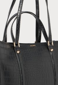 Black crocodile-embossed tote bag with dual handles, gold-tone hardware accents, and a brand logo. Structured design with a smooth texture.