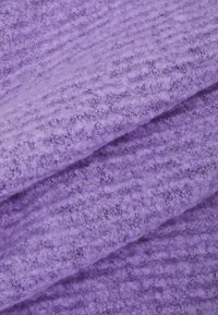 Gros plan sur un tissu violet doux et texturé avec un motif côtelé duveteux et des plis diagonaux.