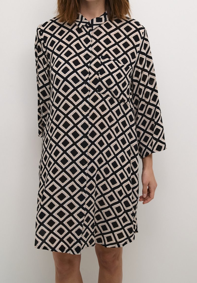 Kortærmet kjole i sort og beige med diamantmønster, med knaplukning foran og krave samt en brystlomme på venstre side.