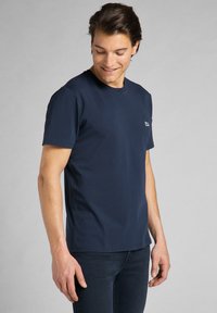 T-shirt in cotone blu navy con maniche corte, scollatura rotonda e un piccolo logo sul lato sinistro del petto. Texture liscia e vestibilità classica.