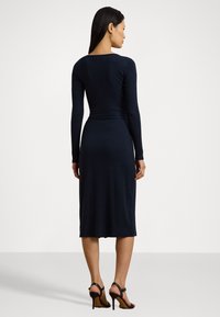 Jūras zila pieguļoša kleita ar garām piedurknēm, taisnu vidēja garuma apakšpusi, apaļu izgriezumu un mīkstu, gludu tekstūru. Kombinēta ar strīpām augstiem papēžiem.