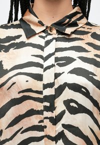 Siidist pluus musta ja beeži tiigririba mustriga, millel on klassikaline krae ja kaelusel peen nööbikujundus.