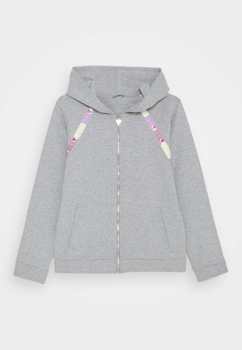 Sweat à capuche gris clair zippé avec poches à l'avant et cordons jaunes, arborant le texte "GUESS" en rose et des logos triangulaires.