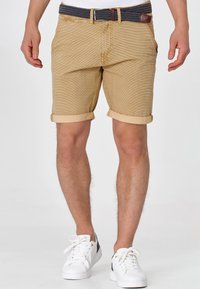 Shorts beiges à motifs avec revers roulés, complétés par une ceinture tressée foncée. Associés à des baskets blanches pour un look décontracté.
