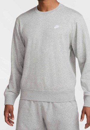Homme portant un sweat-shirt Nike gris clair et un pantalon de survêtement assorti, montrant le haut du torse et les bras, avec un petit logo Nike blanc sur la poitrine.