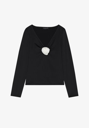 Crni dugi rukav majica s dubokim V-izrezom i bijelim tekstilnim ružom kao naglaskom u sredini. Glatka tekstura s prilagodljivim siluetom.