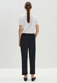 Vit kortärmad skjorta och svarta formella byxor med rak skärning och sidofickor, sedda bakifrån mot en ljus bakgrund.