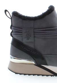 Bota de cuero gris hasta el tobillo con borde de piel sintética, logotipo en relieve y acentos metálicos. Presenta una suela texturizada y detalles de cordones.