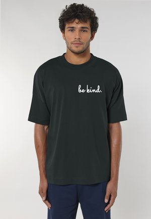 T-shirt nera in cotone con una vestibilità ampia e maniche corte, decorata con testo bianco "be kind." stampato sul fronte. Design casual, texture morbida.