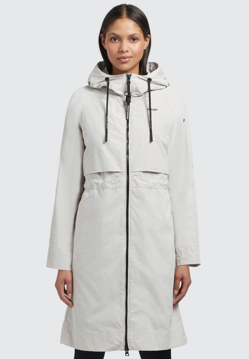 Lichtgewicht, lange witte regenjas met een capuchon, voorritssluiting en zwarte trekkoorden. Heeft een cropped ontwerp en zijzakken.