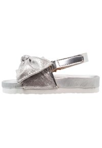 Srebrne metaliczne sandały z akcentem w postaci kokardy, z płaską podeszwą i regulowanym paskiem. Gładka tekstura i minimalistyczny design.