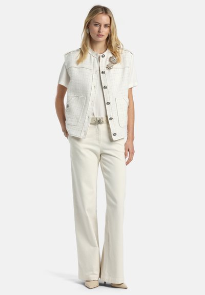 Witte tweedvest met een ronde hals, twee voorzakken en zilveren knopen. Gecombineerd met crèmekleurige wijde broekspijpen en beige puntige schoenen.