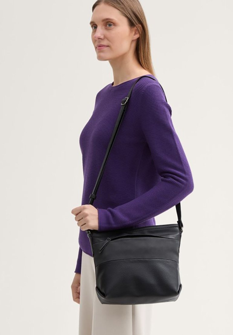 Schwarze Leder-Crossbody-Tasche mit strukturierter Form, mit Zipverschluss oben und kontrastierenden strukturierten Akzenten, präsentiert mit einem lila Oberteil.