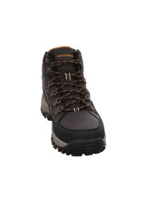 Botas de senderismo marrones con un upper texturizado, puntera de goma y cordones naranjas en contraste. Presenta ojales de metal y una suela robusta.