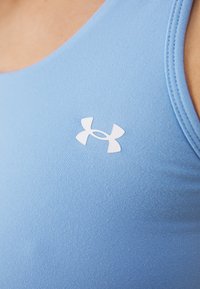 Primo piano di una persona che indossa una canotta da atletica azzurro chiaro con il logo bianco Under Armour sul petto.