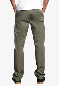 Khakihosen mit geradem Schnitt, Mischmaterial aus Baumwolle, sichtbaren Gesäßtaschen und leichtem Glanz; kombiniert mit schwarzen Schuhen mit Gummisohlen.