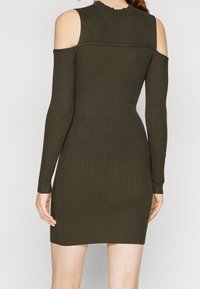 Geripptes, olivgrünes Kleid mit langen Ärmeln und schulterfreiem Design. Es zeichnet sich durch eine taillierte Form und eine strukturierte Stoffoberfläche für zusätzliche Details aus.