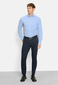 Camicia azzurro chiaro con bottoni, maniche lunghe, taschino sul petto; abbinata a pantaloni slim-fit blu navy scuri e scarpe in pelle nera. Design semplice e classico.