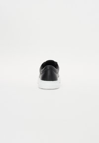 Adidași din piele neagră cu o textură netedă, talpă din cauciuc alb, formă rotunjită și design minimalist, văzuți din spate.