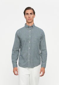 Overhemd met knopen in een groen en marineblauw ruitpatroon, gemaakt van stof met zichtbare textuur, met een kraag en lange mouwen.