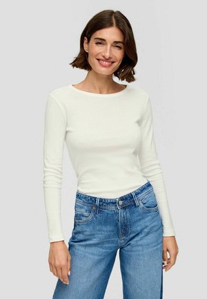 Langärmliges, tailliertes weißes Baumwolloberteil, kombiniert mit hoch taillierten blauen Jeans aus Denim, die fünf Taschen und eine klassische blaue Waschung aufweisen.