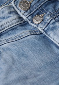 Lichtblauwe denimstof met twee metalen knopen waarop "STREET" is gegraveerd. Zichtbare stiksels en lichte slijtagepatronen.