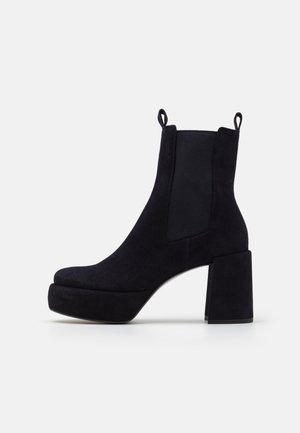 Bottines en daim noir avec un talon épais, panneaux latéraux élastiques et languettes pour un enfilage facile. Tige texturée et semelle plateforme.