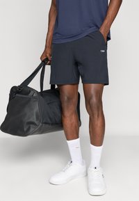 Vyriški sportiniai šortai iš tamsiai mėlynos medžiagos, su logotipo detale, su reguliuojamu juosmeniu. Nepakartojamai derinami su baltais sportbačiais ir juodu sportiniu krepšiu.