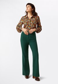 Multicolored blouse with a floral pattern, button-up front, and puffed sleeves paired with high-waisted, straight-leg green trousers.