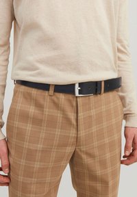 Beige kötött pulóver barna kockás nadrággal, ami finom ellenőrző mintázattal rendelkezik, és egy sötétkék bő övvel, amely ezüst szögletes csattal van ellátva.