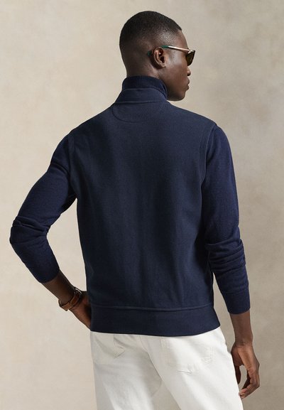 Pull-over bleu marine avec un col montant, des manches longues et des poignets côtelés. Confectionné en tissu tricoté doux, présentant une texture lisse et une coupe ajustée.