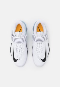 White athletic shoes with a black swoosh, mesh upper, adjustable strap, padded collar, and orange accents on the insoles.