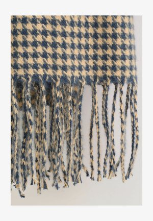 Bela in bež houndstooth vzorec volnene šal z zavitimi resicami, ki vise proti svetli ozadju.