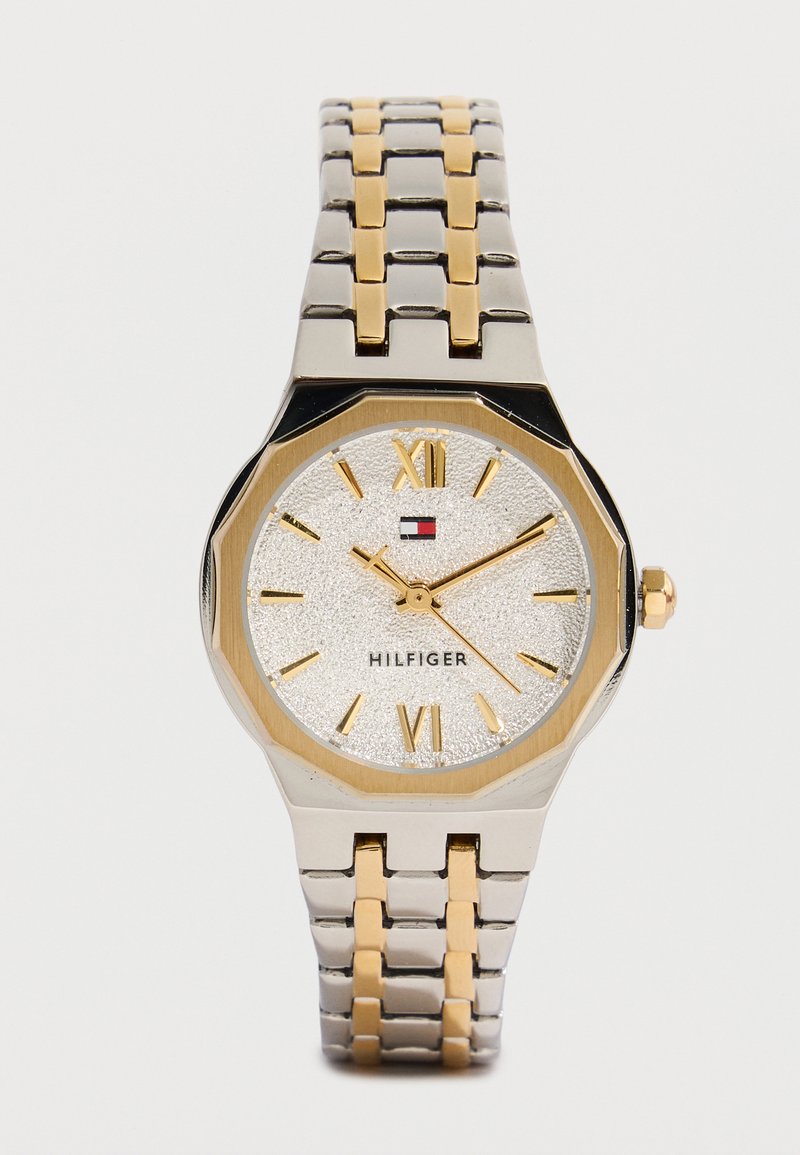 Ρολόι χειρός από ασημένιο και χρυσό μέταλλο με υφή ασημένιου καντράν, χρυσούς λατινικούς αριθμούς και το λογότυπο Tommy Hilfiger κάτω από τις 12.