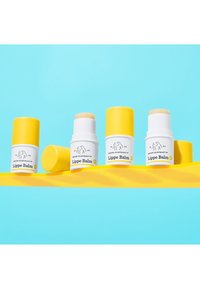 Drei Lippenbalsam-Röhrchen horizontal angeordnet. Zwei sind weiß mit gelben Kappen; eines ist fest gelb. Alle zeigen Text mit dem Produktnamen.