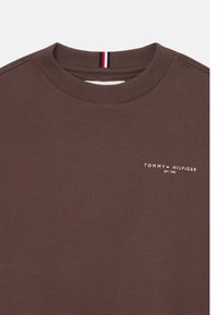 Brun sweatshirt med ribbet krave. Har et lille hvidt "TOMMY HILFIGER" logo og teksten "EST. 1985" på brystet. Blød tekstur.